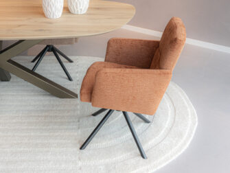 Luxe eetkamerstoel in koperkleurige zachte stof met armleuningen en een zwarte draaipoot